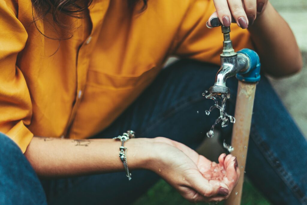 Close-up of a woman collecting water from an outdoor faucet, wearing a bracelet.
